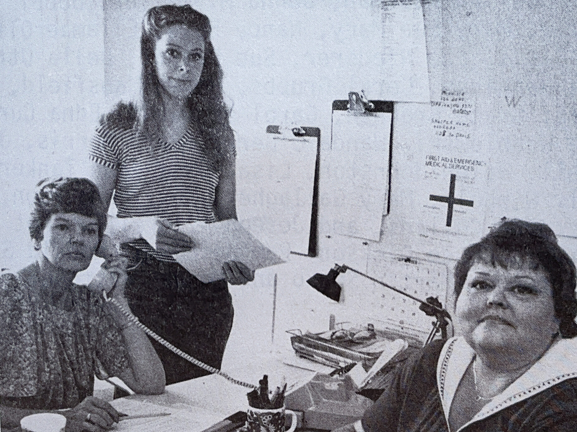 Mary Henderson sits at a desk with two volunteers